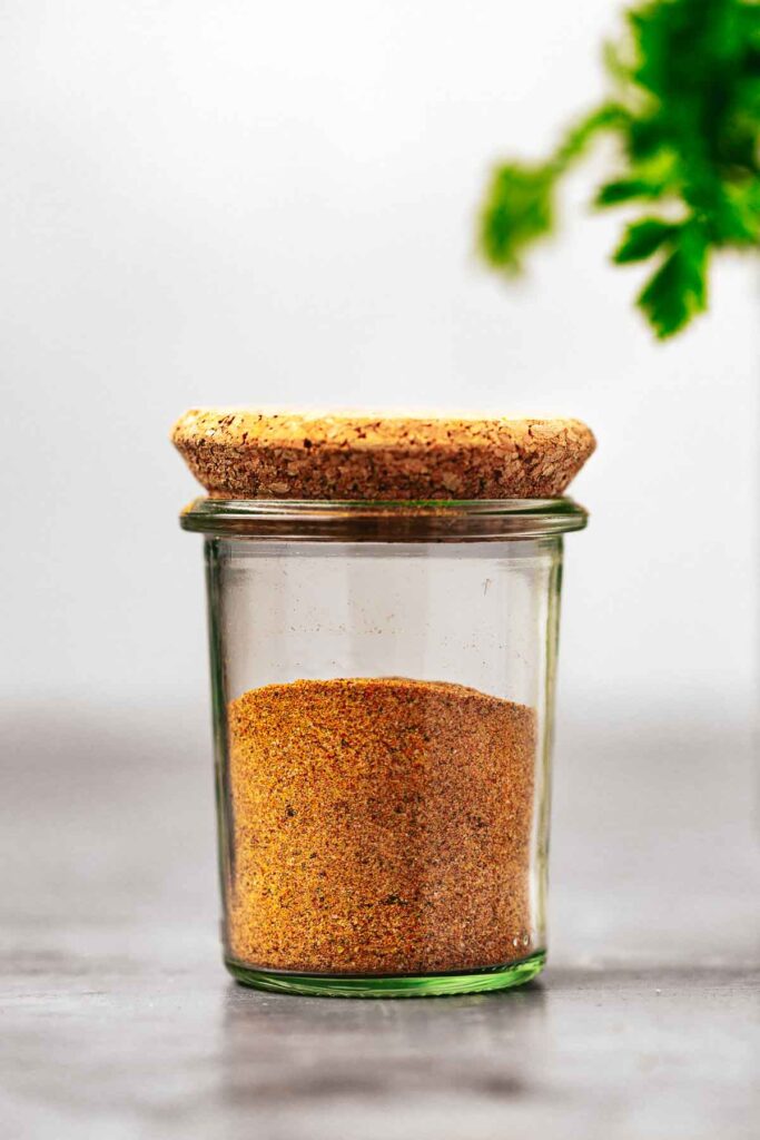 A glass spice jar with a cork lid, filled with seasoning mix