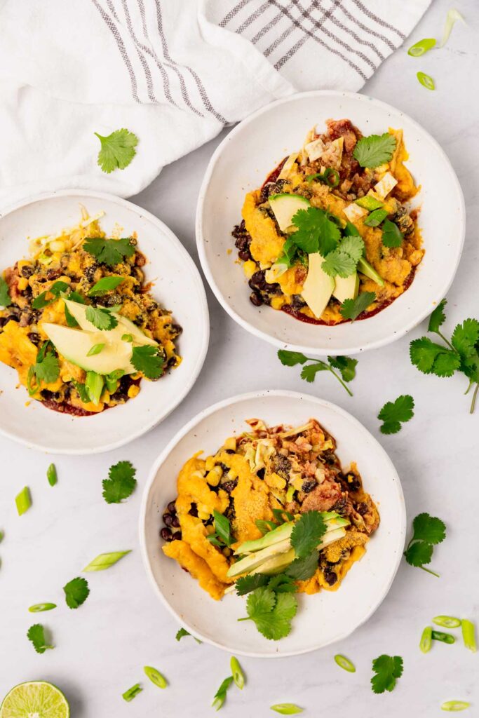 Three bowls of vegan enchilada casserole topped with avocado slices and cilantro.