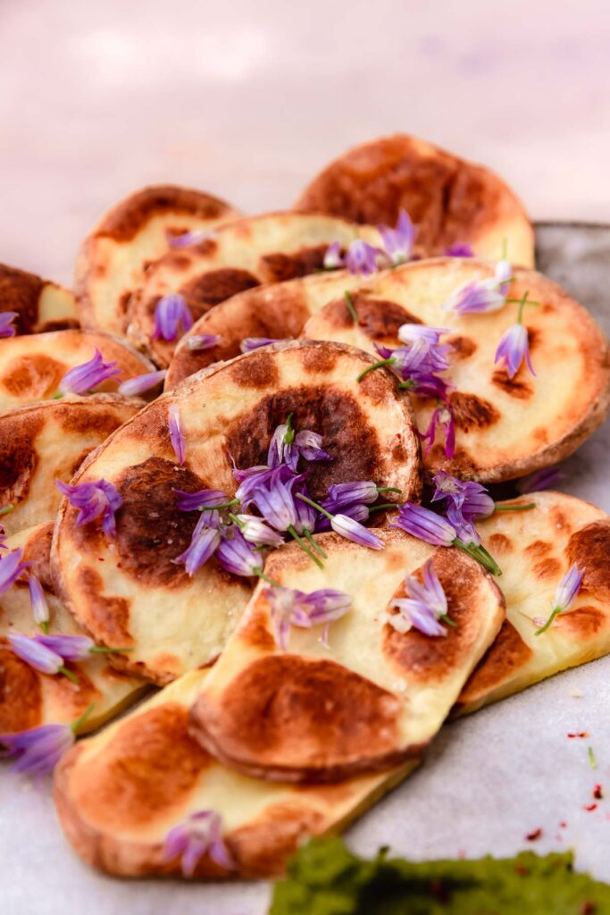 Roasted potato slices topped with purple chive flowers.