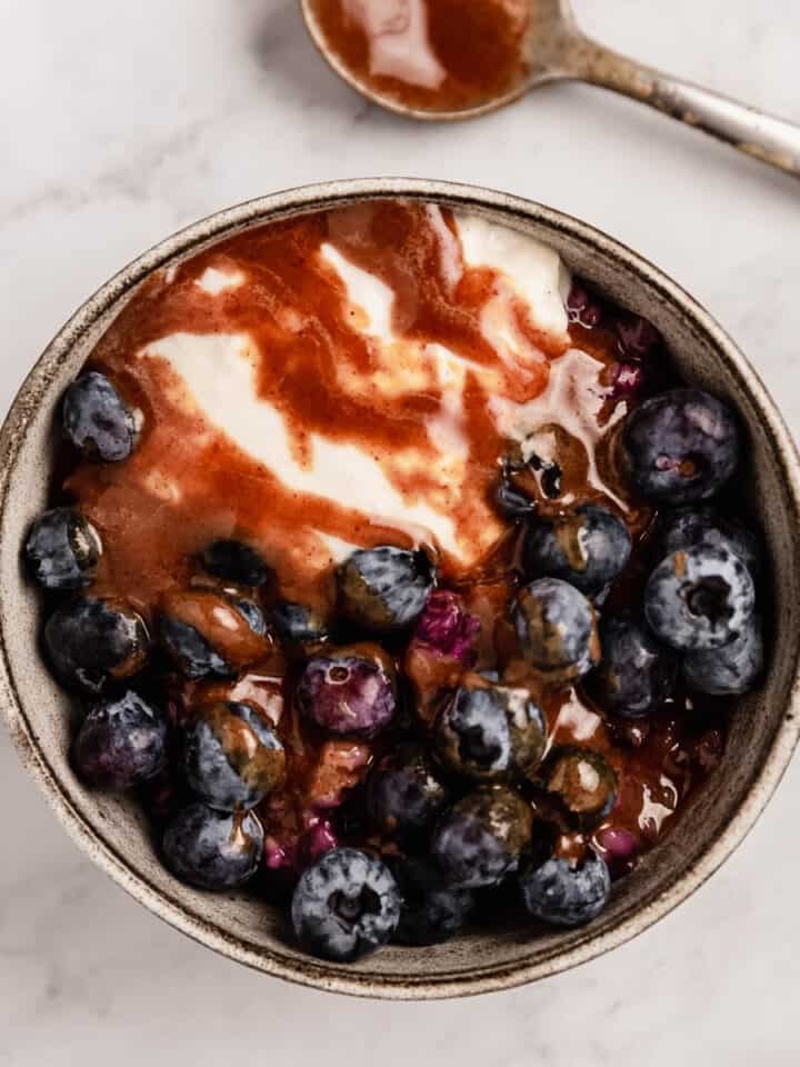 A bowl of berry porridge with fresh blueberries, yogurt, and homemade caramel sauce.