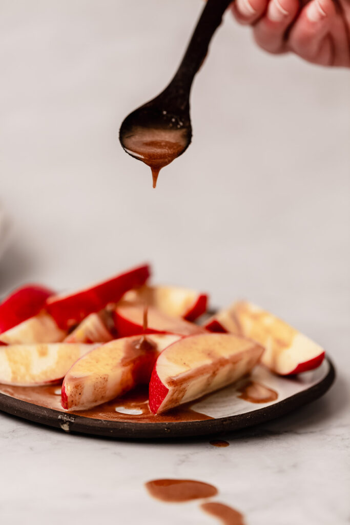 Vegan caramel sauce being drizzled off a spoon over sliced red apples on a plate.