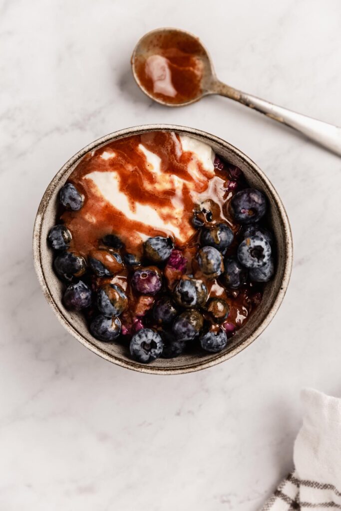 A bowl of berry oatmeal covered with blueberries, yogurt, and caramel sauce.