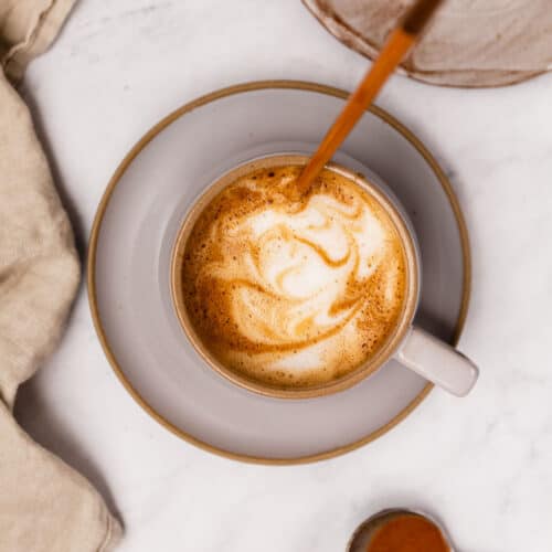 An overhead view of a chopstick creating designs in the foam of a latte.