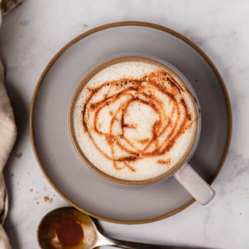 Steamed milk topped with caramel swirls in a gray cup.