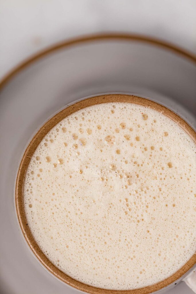 A closeup overhead view of caramel-colored steamed milk in a cup.