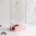 Cherries at the bottom of a pitcher with water pouring into it.