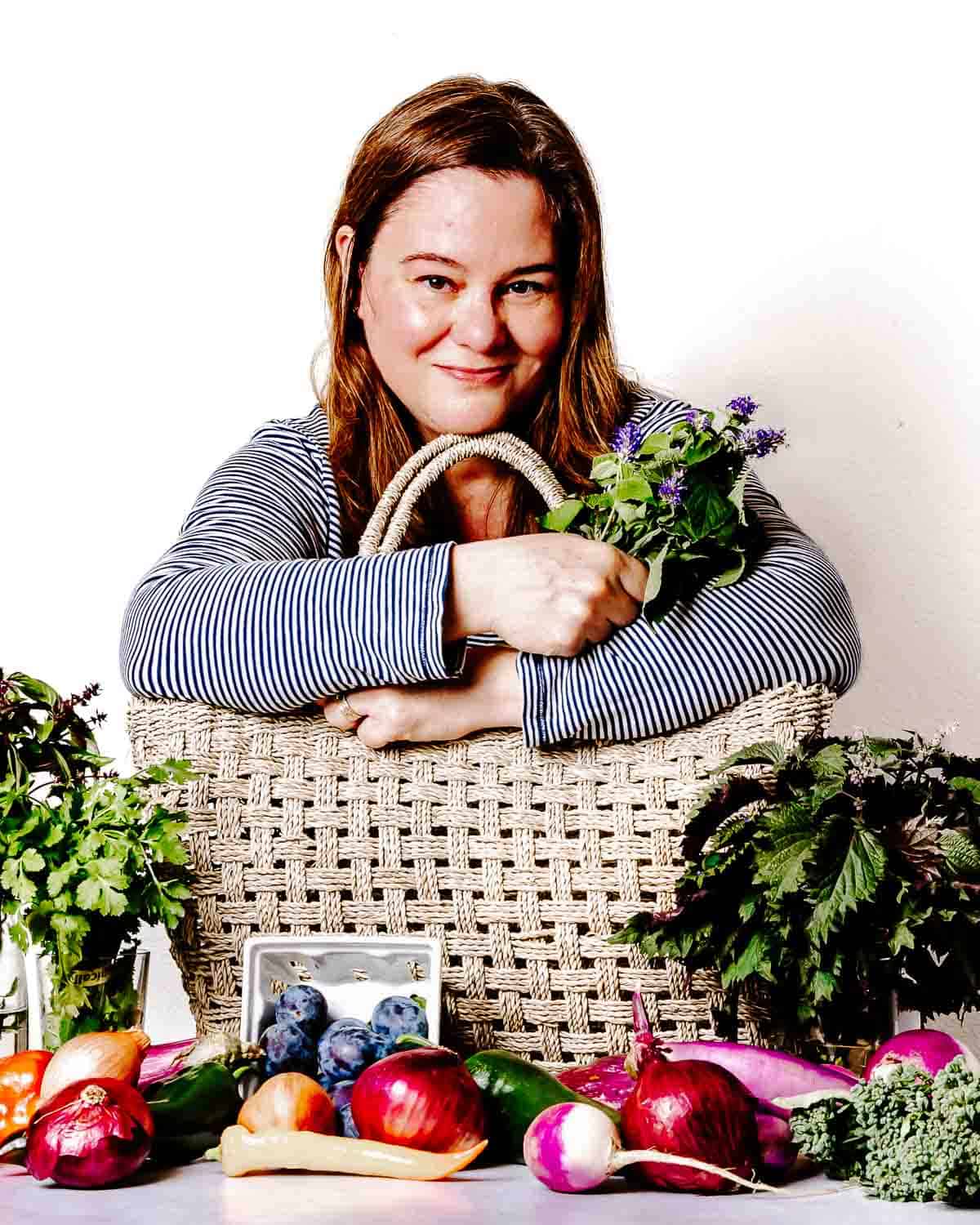 Kari hugging her market basket while surrounded by fresh produce.