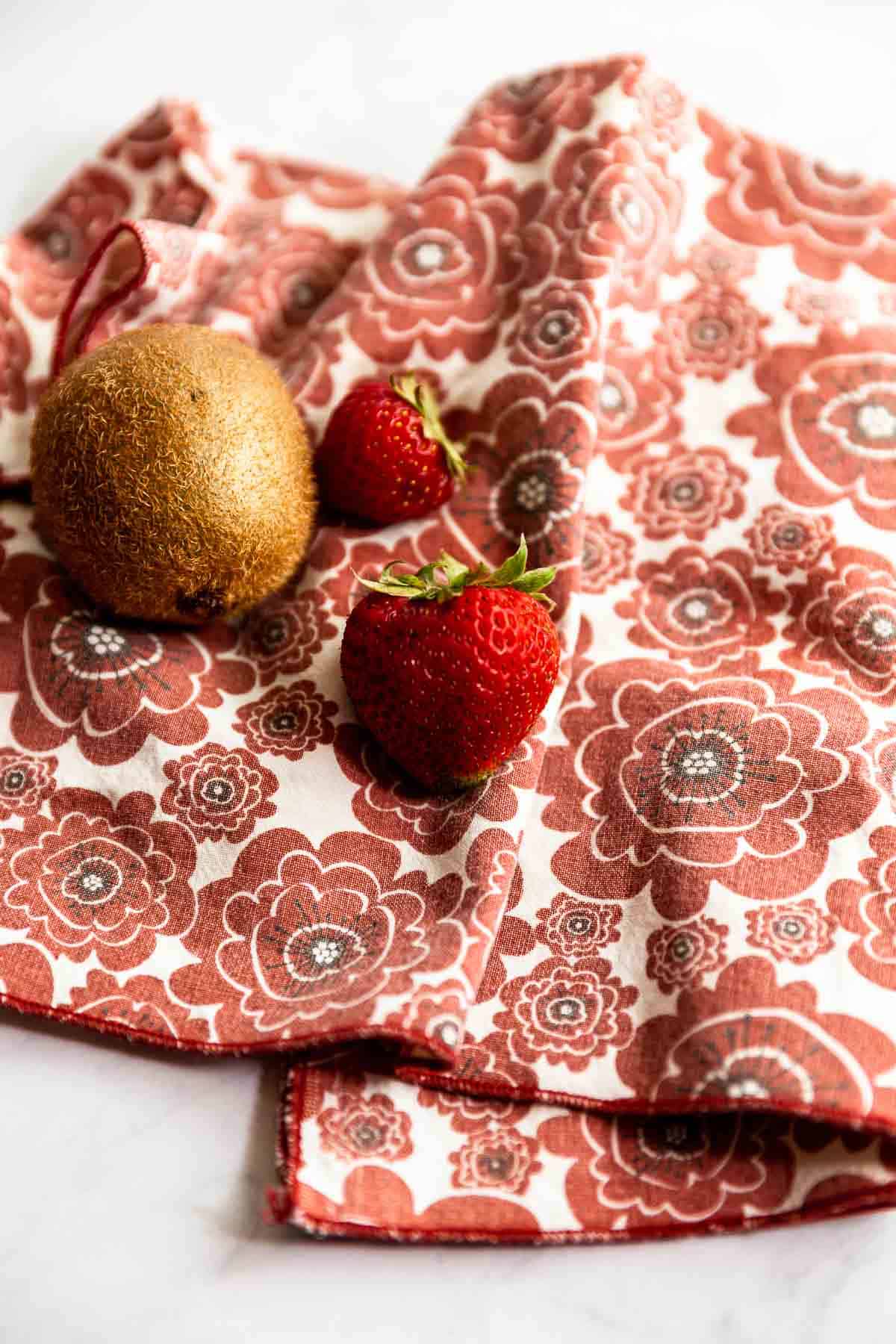 A couple strawberries and a kiwi laying on a red floral napkin.
