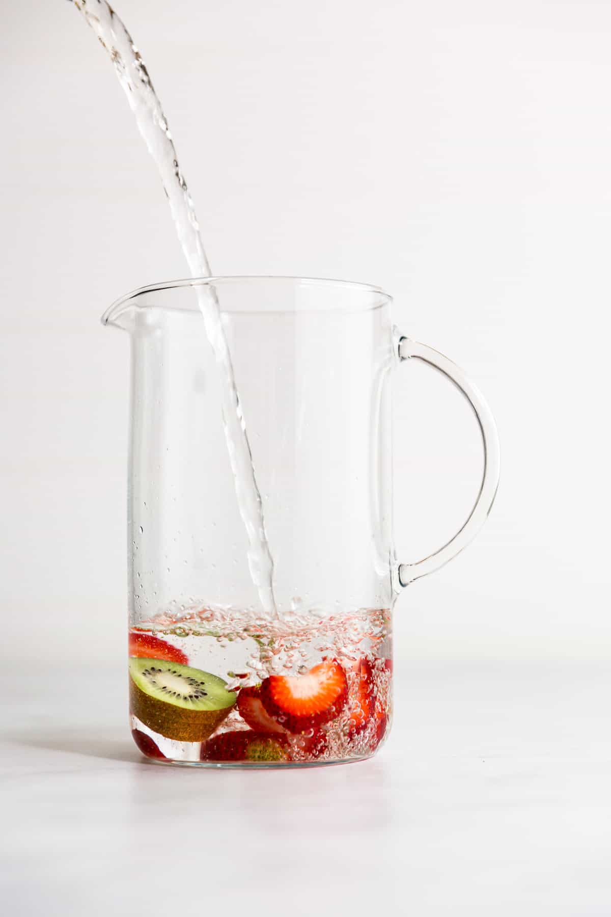 A glass pitcher partly filled with water with strawberries and kiwi slices floating in it.
