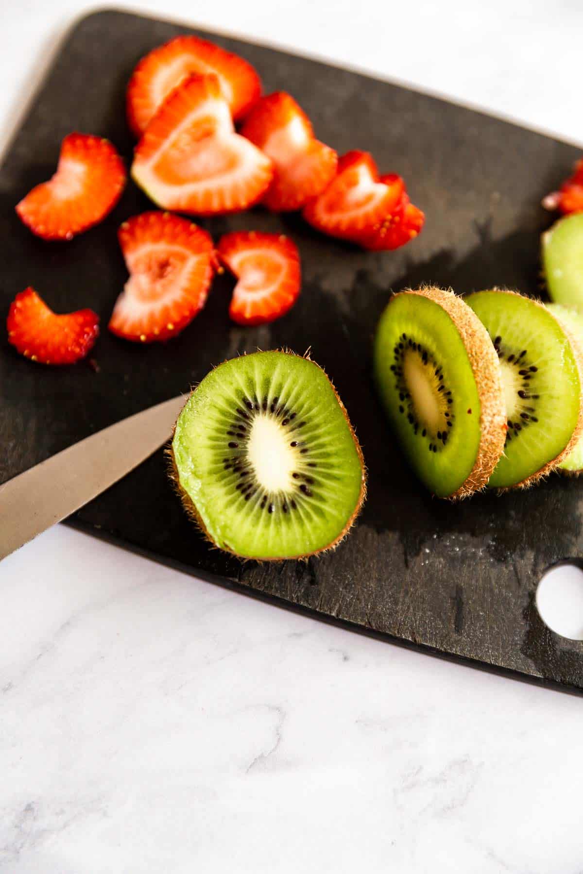 Slices of kiwi and strawberries on a black cutting board.