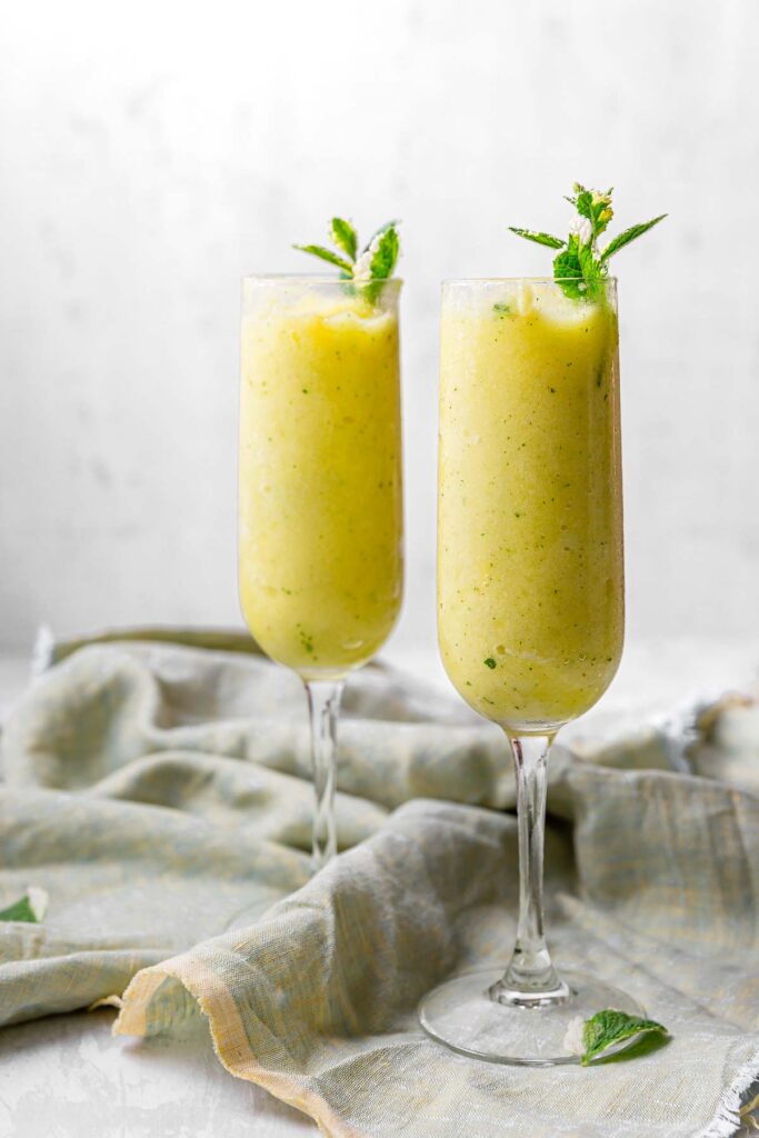 Two tall glasses filled with frozen pineapple mint cocktails, topped with fresh pineapple mint.