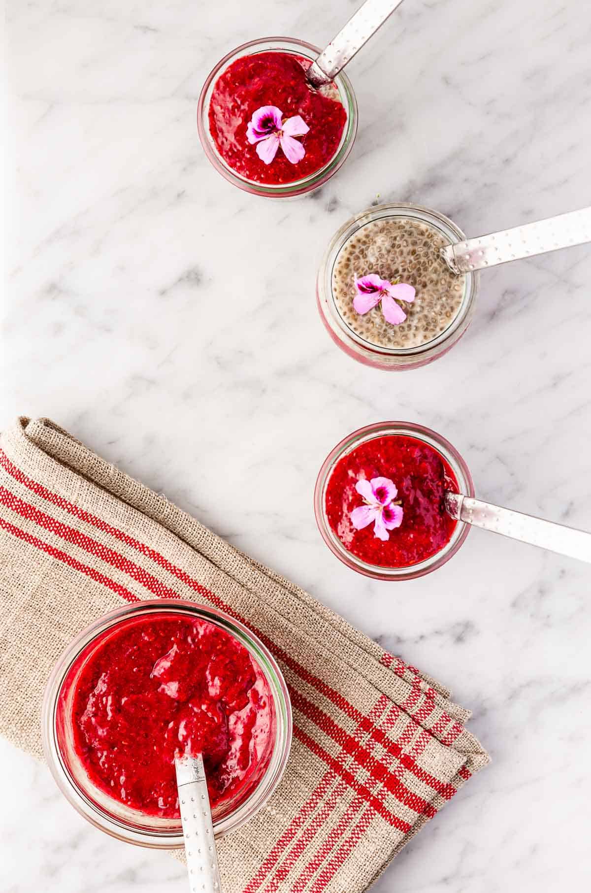 A jar of chia jam on a red striped napkin surrounded by three smaller jars of chia pudding with the jam in them.