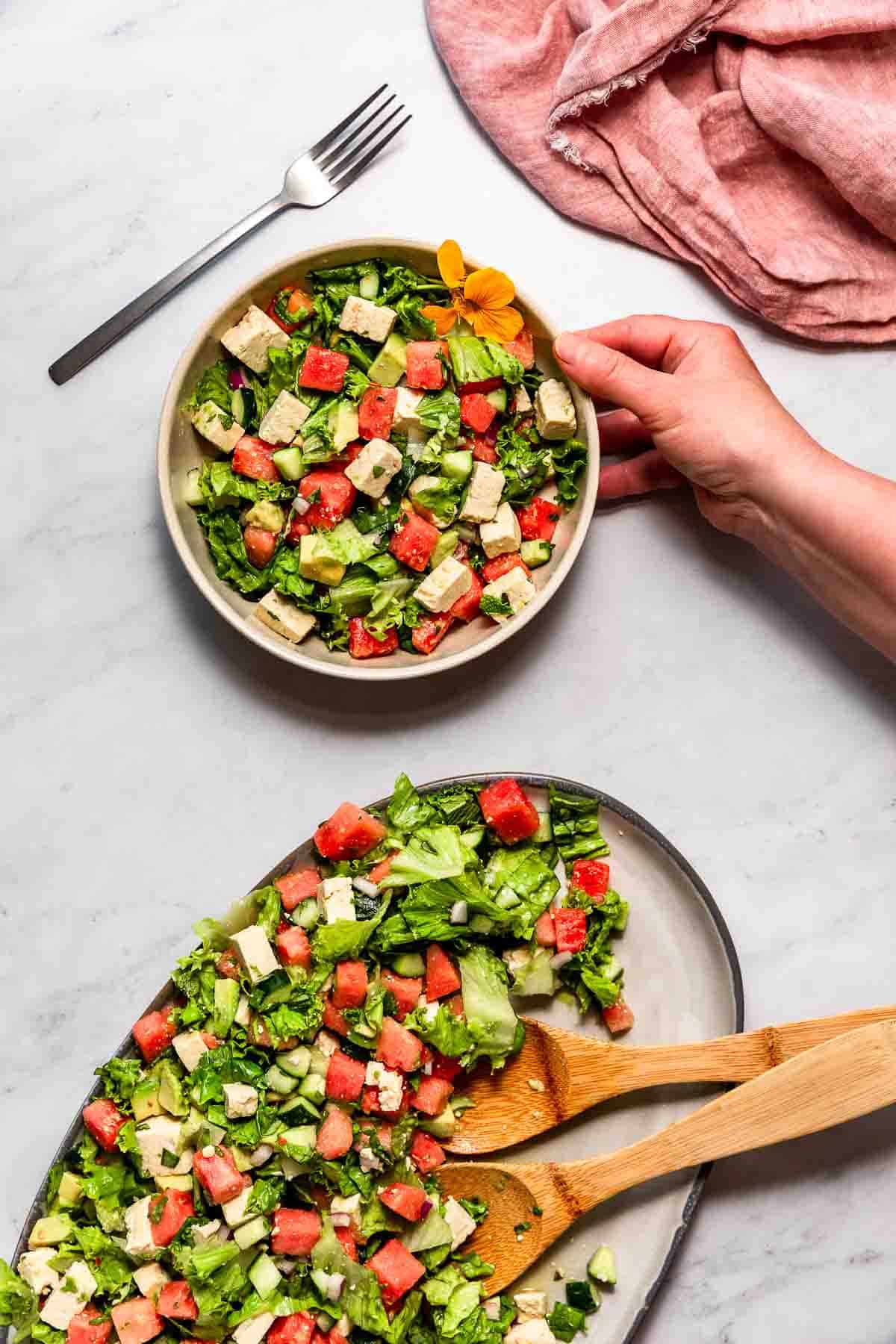 A grey platter filled with watermelon salad on a marble surface.