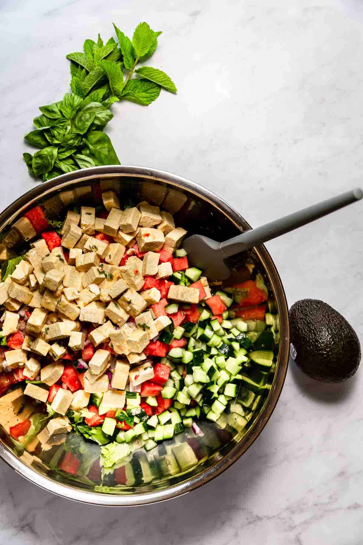 A large stainless bowl of salad ingredients with tofu feta on top.