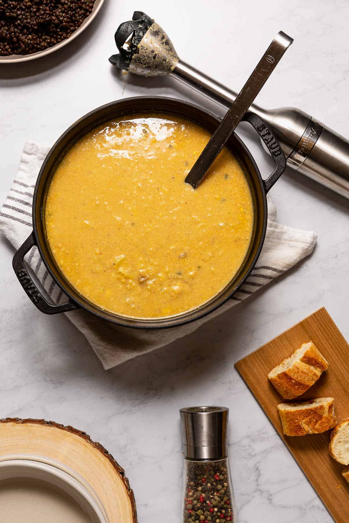 A large pot full of creamy Easy Homemade Vegan Potato Corn Chowder with an immersion blender behind it.