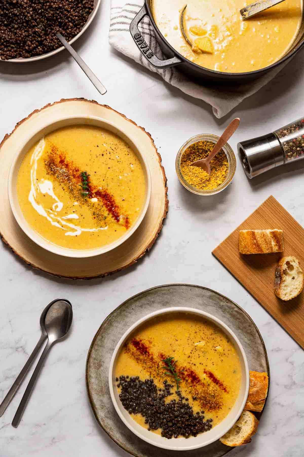 Two bowls of homemade vegan potato corn chowder topped with spices and black lentils with a side of sourdough.