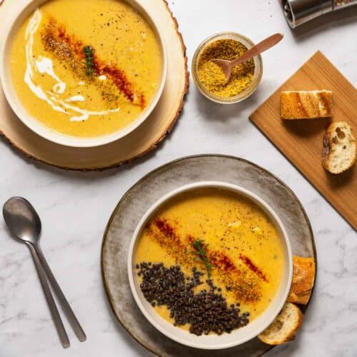 A close-up view of two bowls filled with homemade vegan potato corn chowder with toppings on a marble surface.