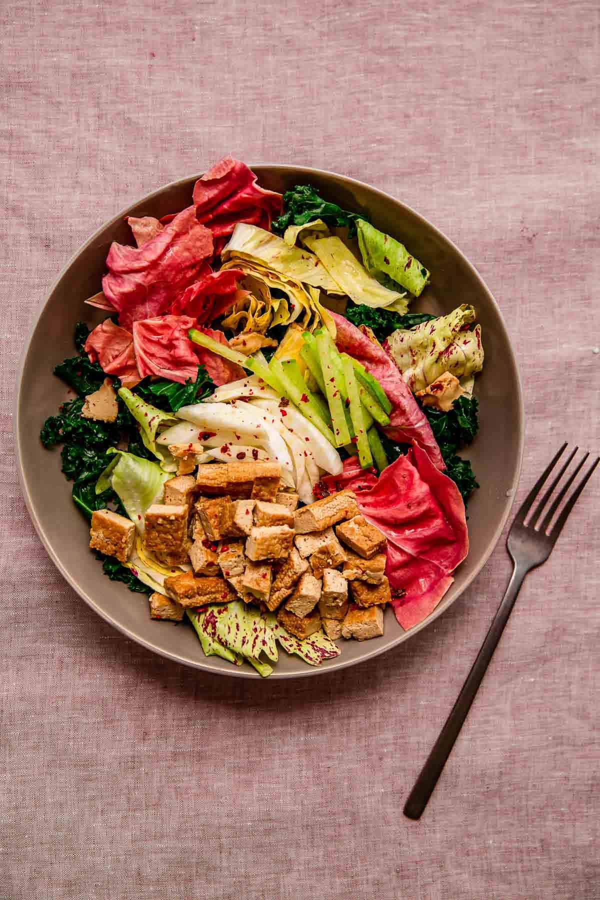 A big beautiful bowl of colorful salad, with pink and green veggies and steamed tofu - all on a faded pink linen.