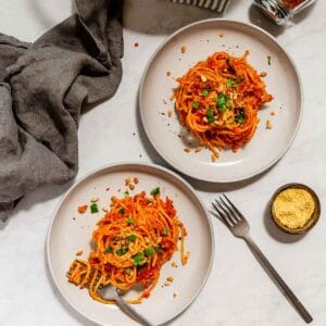Easiest vegan red lentil bolognese spaghetti on two plates, with one fork twirling noodles.