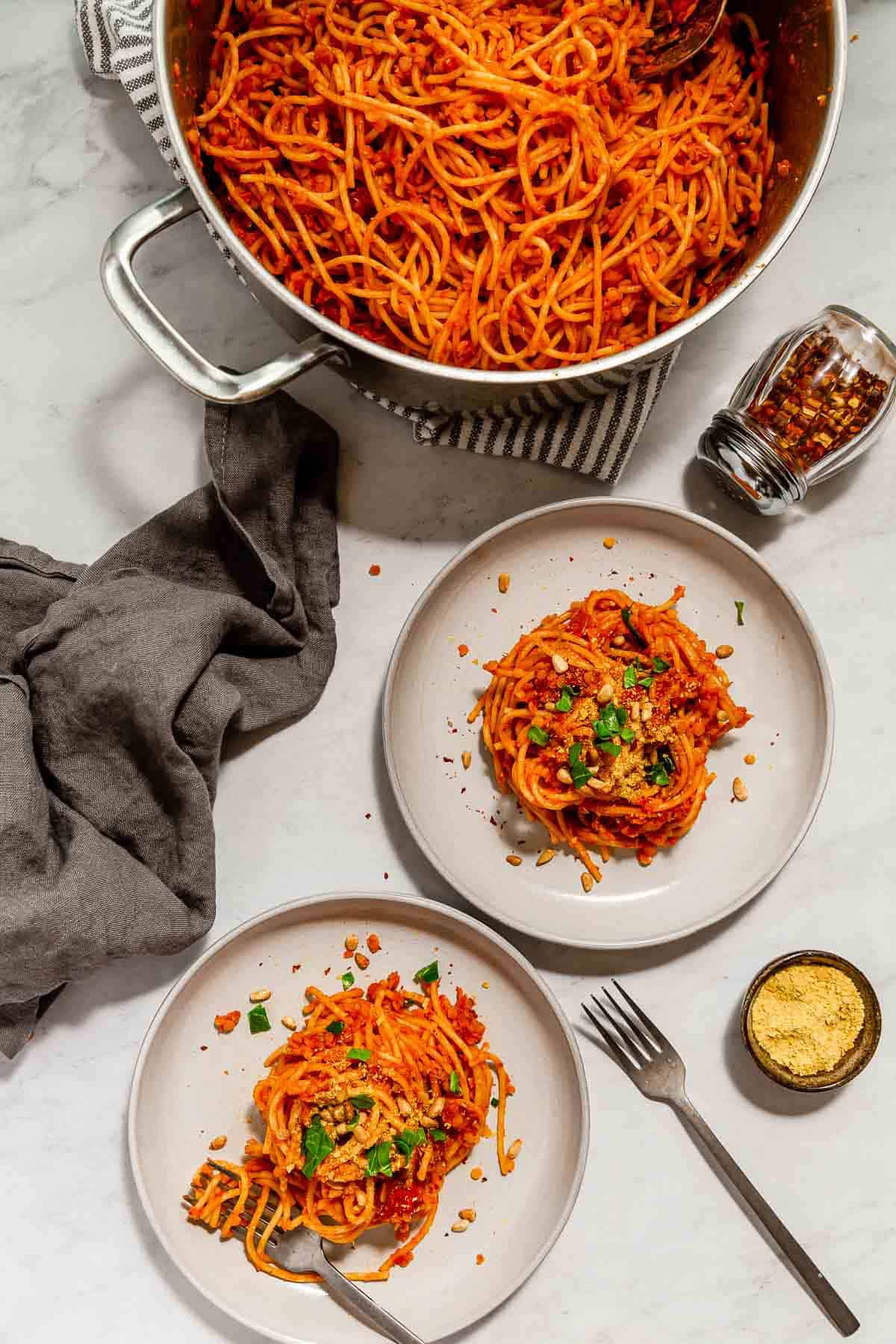 Vegan red lentil bolognese on two plates, topped with pine nuts, nooch, and chopped greens.