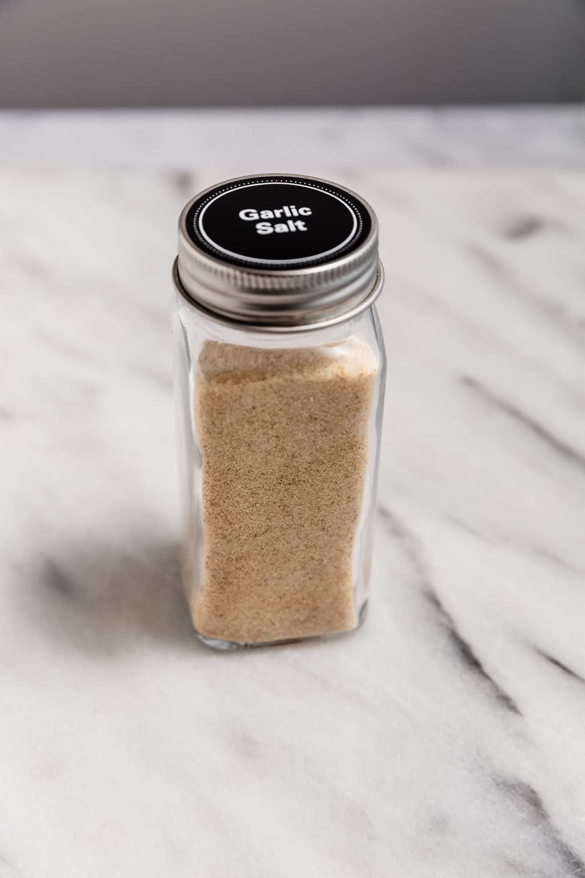 A finished 4-oz jar of homemade garlic salt, with a black label indicating the spice name on the lid.