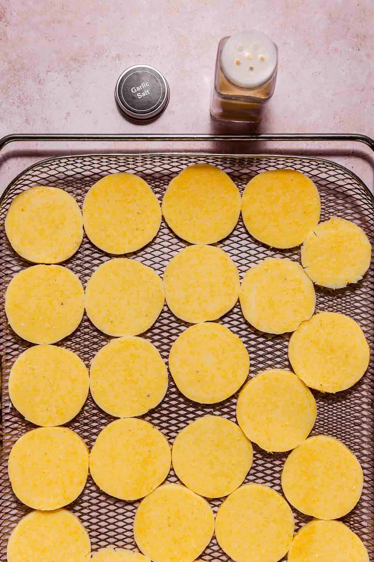 Polenta rounds on an air fryer tray ready to be toasted.