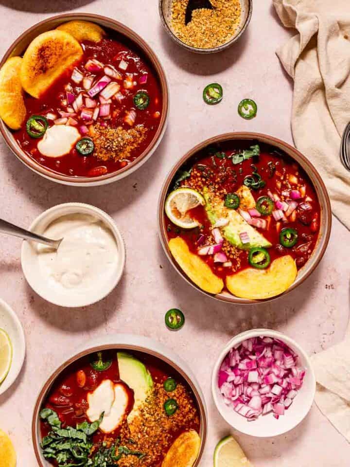Vegan Instant Pot chili with greens served up in three bowls surrounded by topping options.