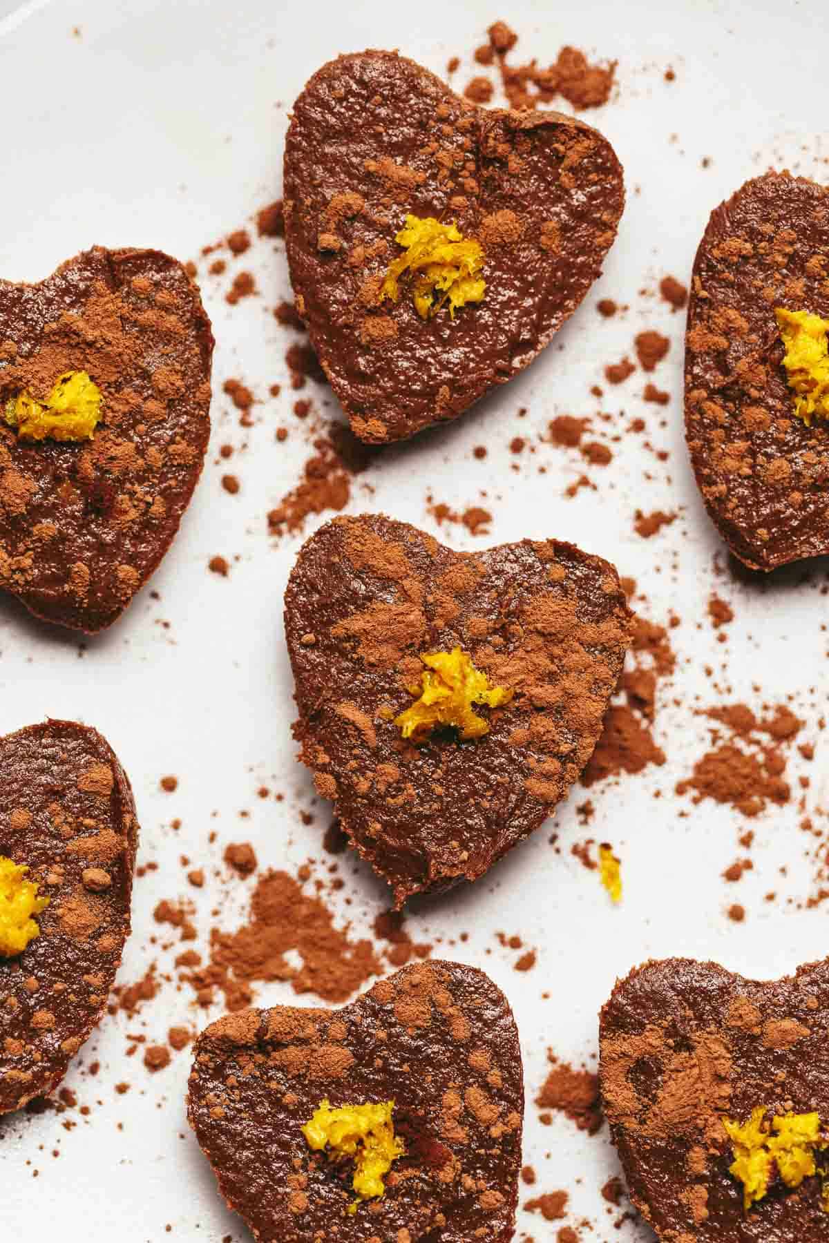 A closeup of several chocolate orange semifreddo hearts topped with cacao powder and orange zest.