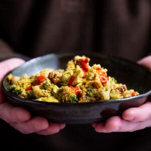 A bowl of vegan broccoli quinoa casserole with white beans, breadcrumbs, and sriracha in a man's hands.