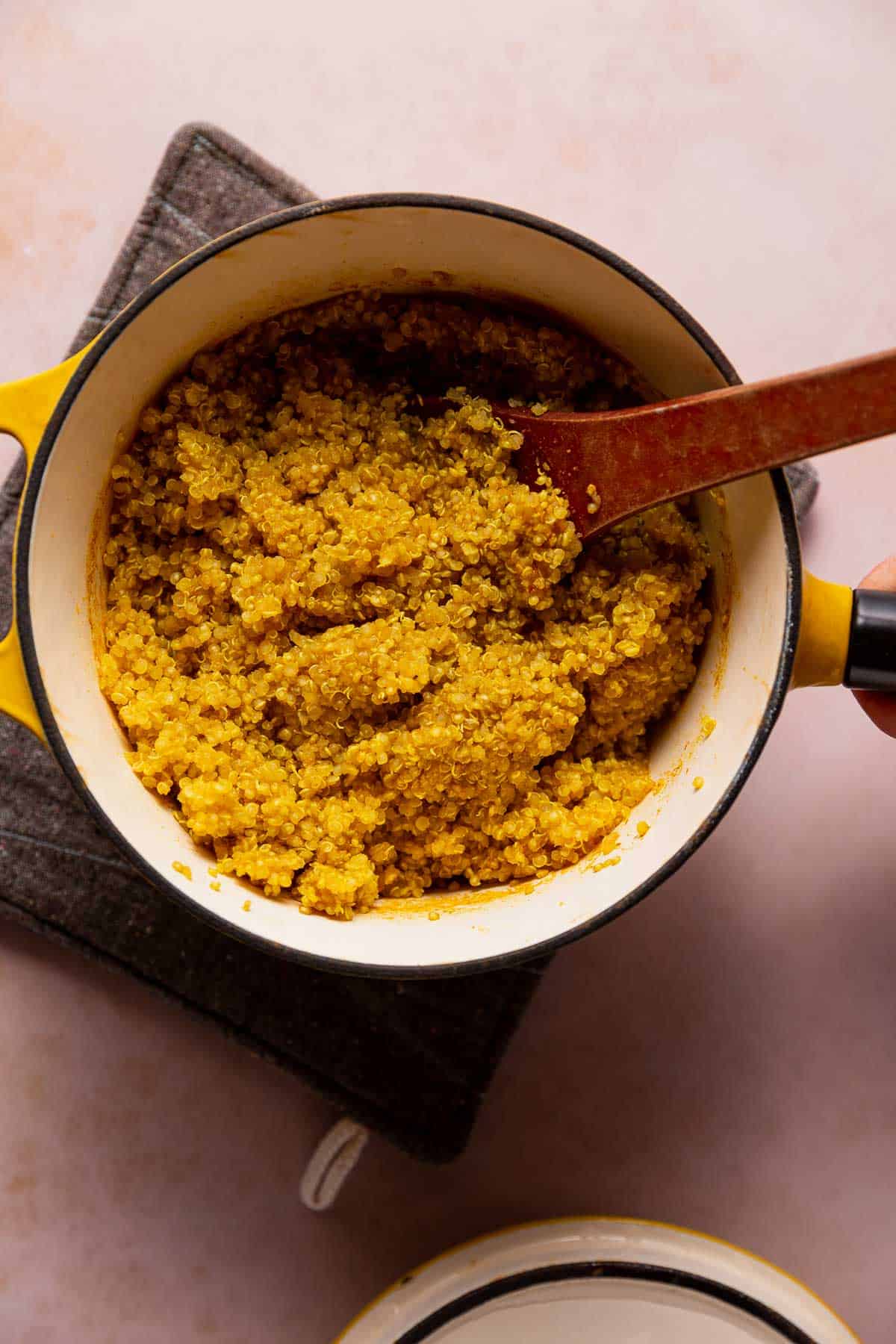 A wooden spoon fluffing up quinoa in a pot.