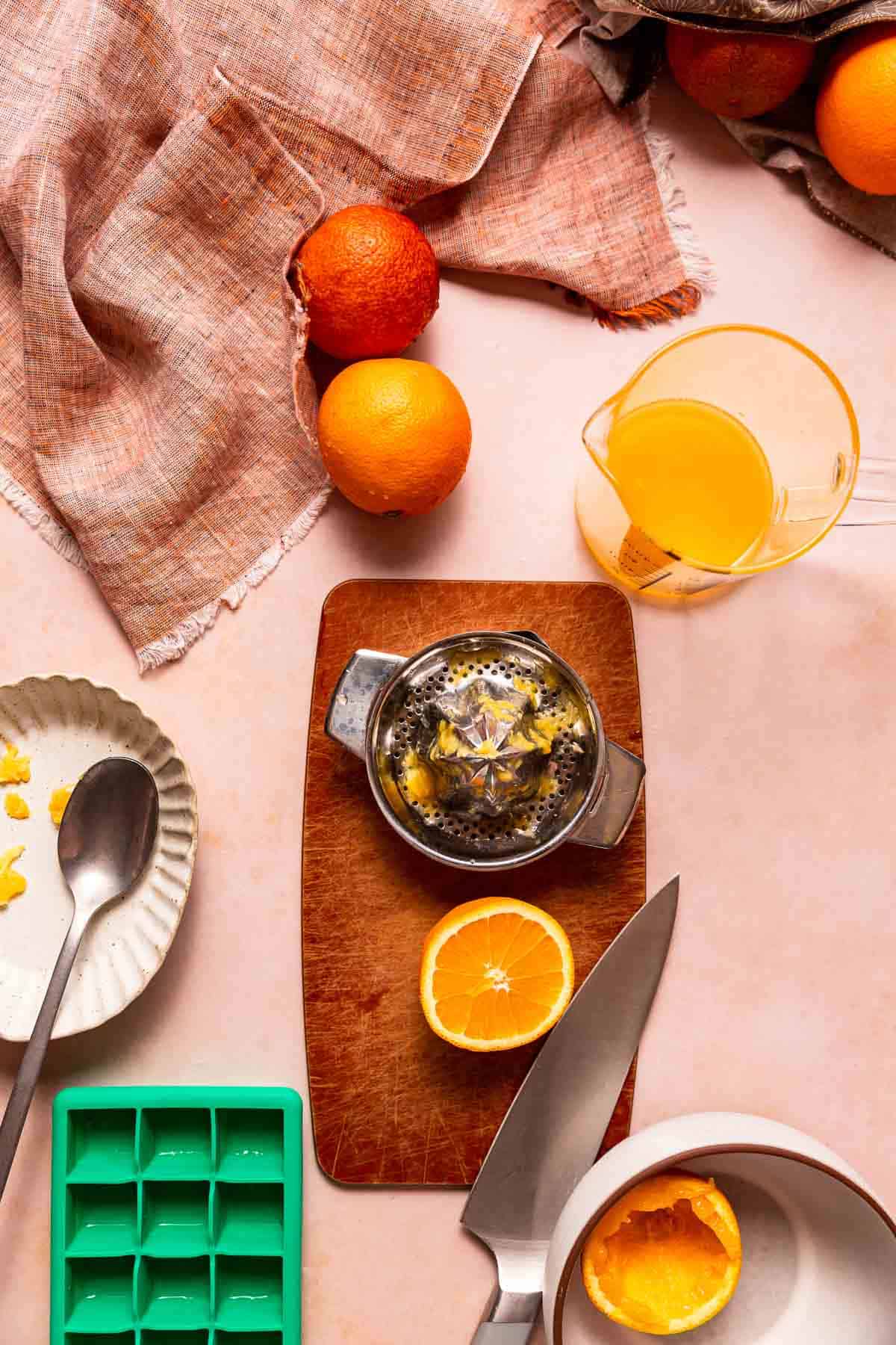 A stainless steel juice reamer next to a sliced orange, a blood orange and orange. and a measuring cup filled part way with fresh squeezed orange juice.