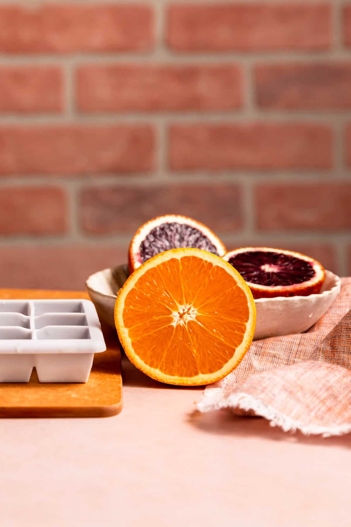Sliced oranges and blood oranges next to an ice cube tray.
