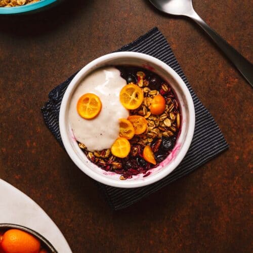 Vegan crisp with berries, sliced kumquats, and yogurt in a white ramekin.