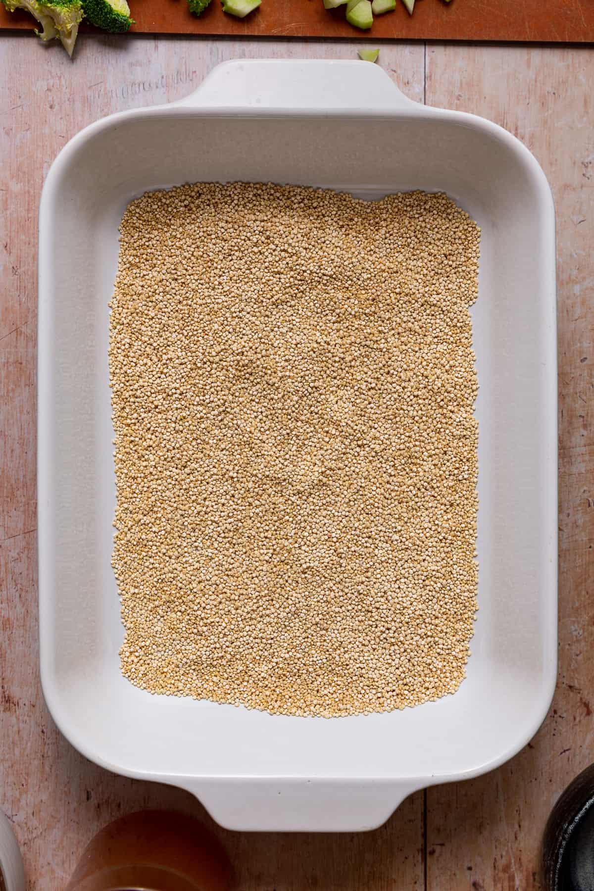 Uncooked quinoa in the bottom of a 9x13 pan for vegan broccoli casserole.