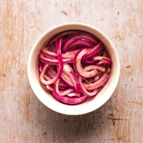 A ramekin filled with pink lime pickled onions on a wood surface.
