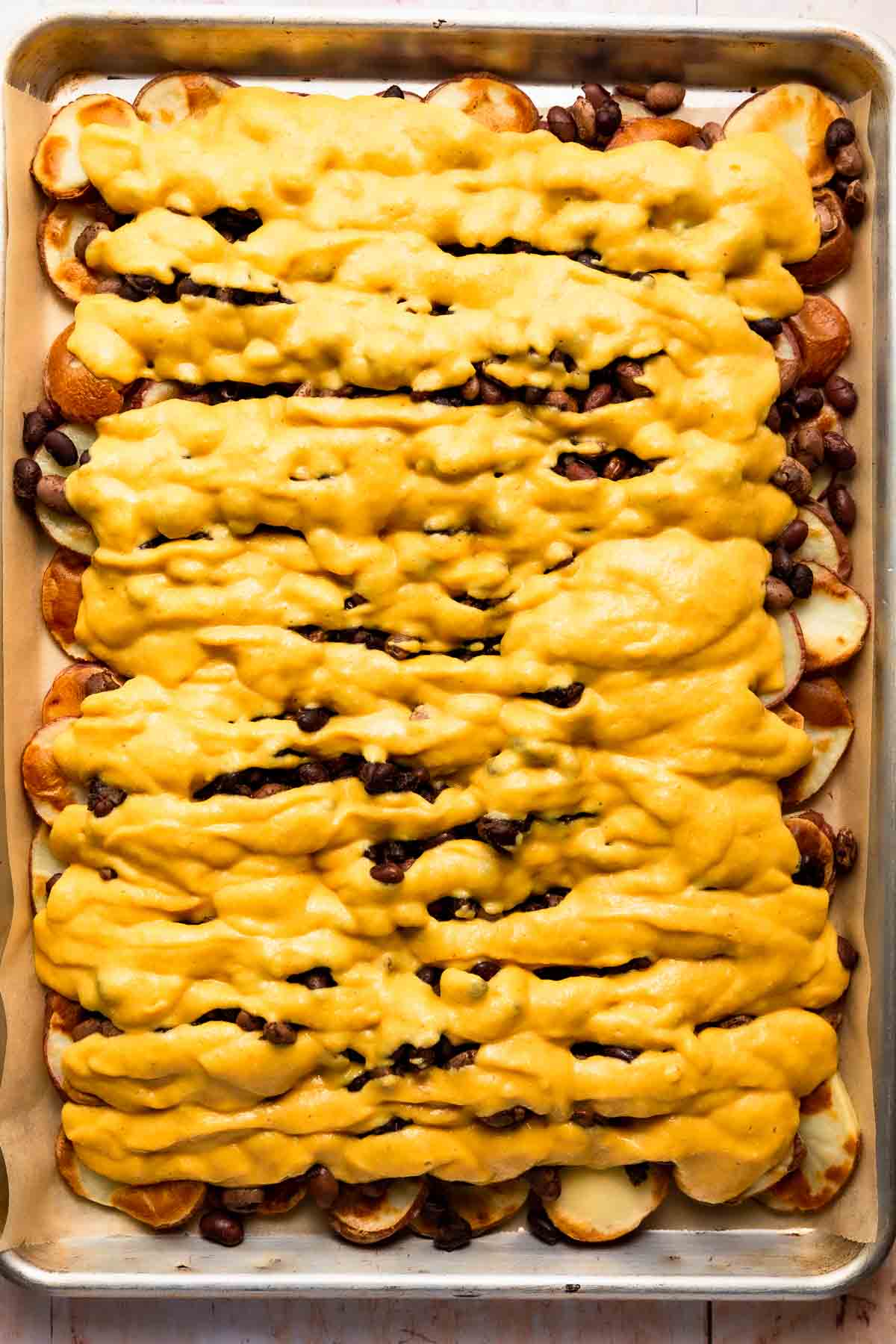 Plant-based queso sauce poured over nachos on a baking sheet.
