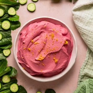 Pink beet hummus filling a large bowl and surrounded by salad ingredients.