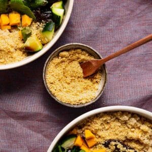 Dairy-free parmesan cheese sprinkles in a small bowl surrounded by large salads.