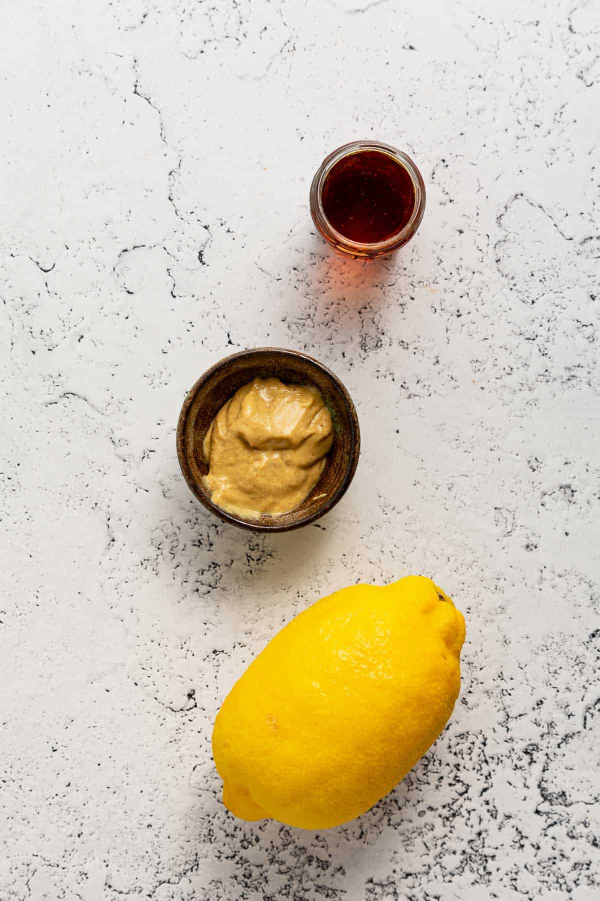 Three ingredients for making maple dijon dressing: a lemon, mustard, and maple syrup.