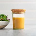 Maple dijon salad dressing in a small jar with a cork lid next to a green salad.