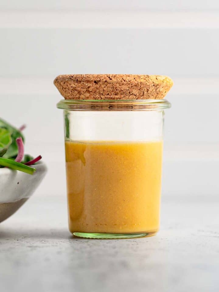 Maple dijon salad dressing in a small jar with a cork lid next to a green salad.
