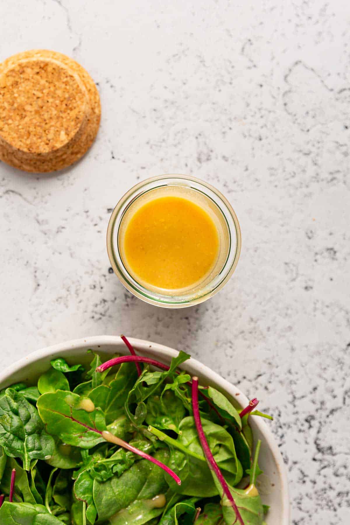 A small jar of maple dijon dressing above a green salad with dressing on it.