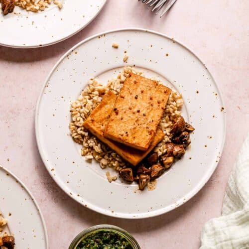 Tofu steaks on top of oat groats, served next to sauteed mushrooms.