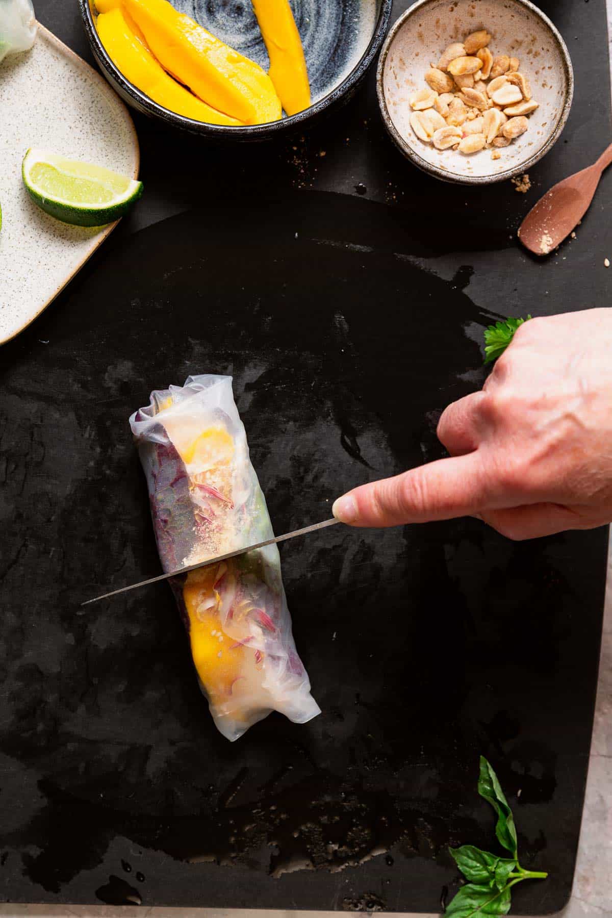A hand slicing a filled summer roll in half.