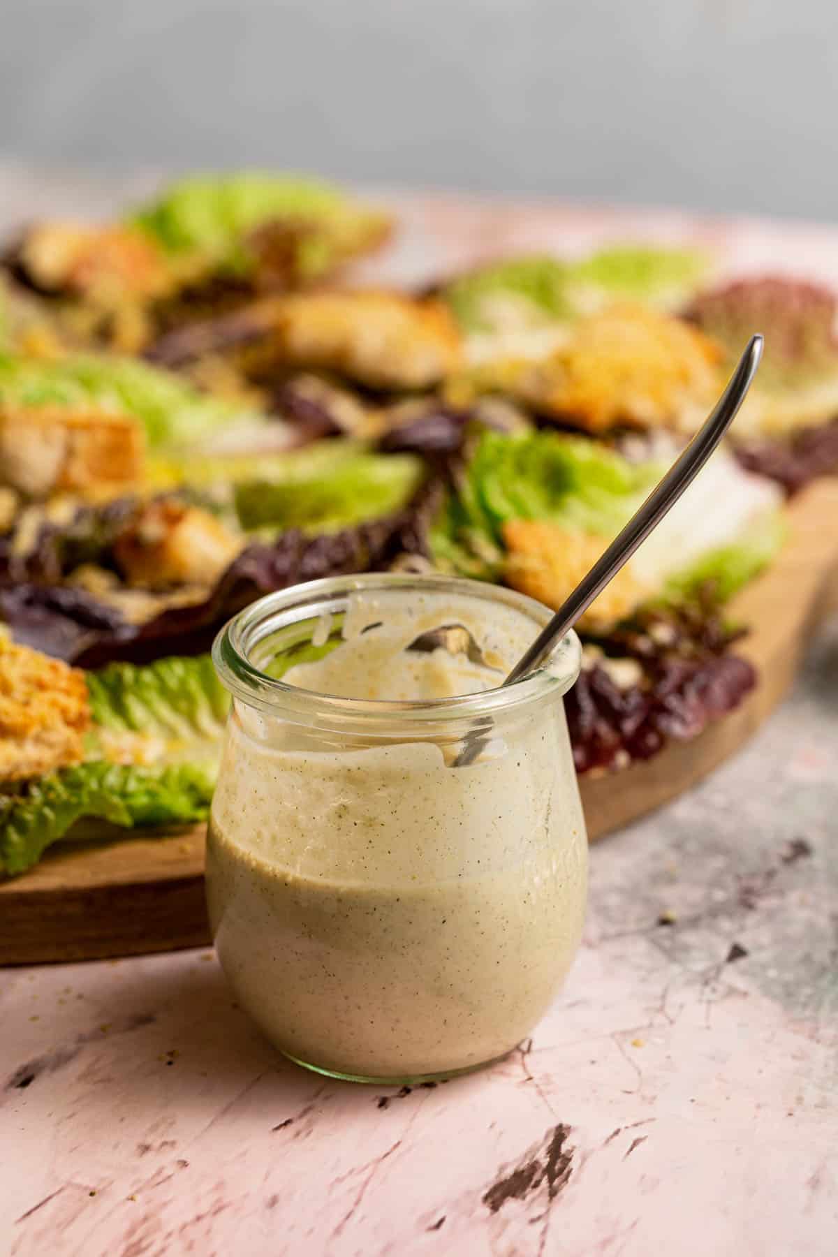 A jar of vegan caesar dressing in front of handheld caesar salads.