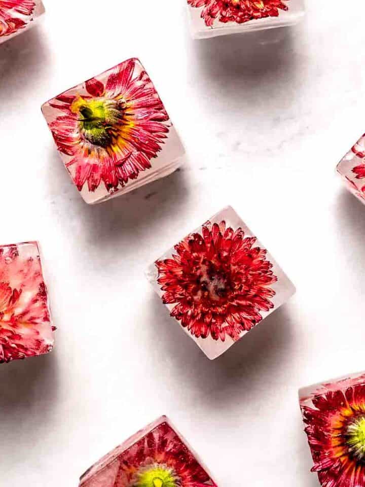 Edible flower ice cubes scattered on a marble surface.