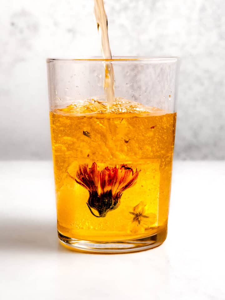 Iced tea being poured into a glass with a floral ice cube in it.