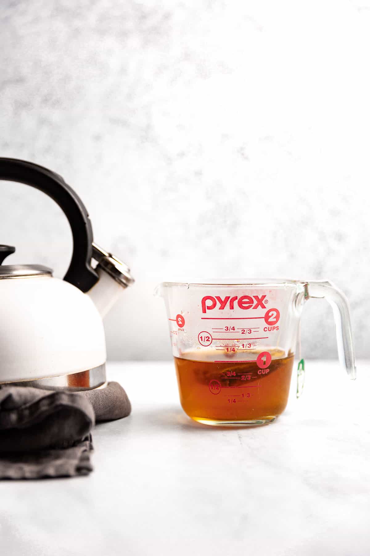 A teabag steeping in a glass measuring pitcher half filled with hot water.