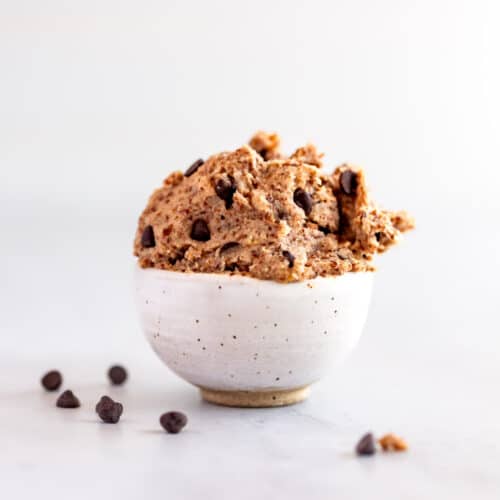 A small bowl of raw vegan gluten-free chocolate chip cookie dough with chocolate chips scattered around it.