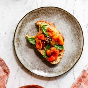 Bruschetta on a handmade plate topped with air fryer cherry tomatoes and fresh basil.